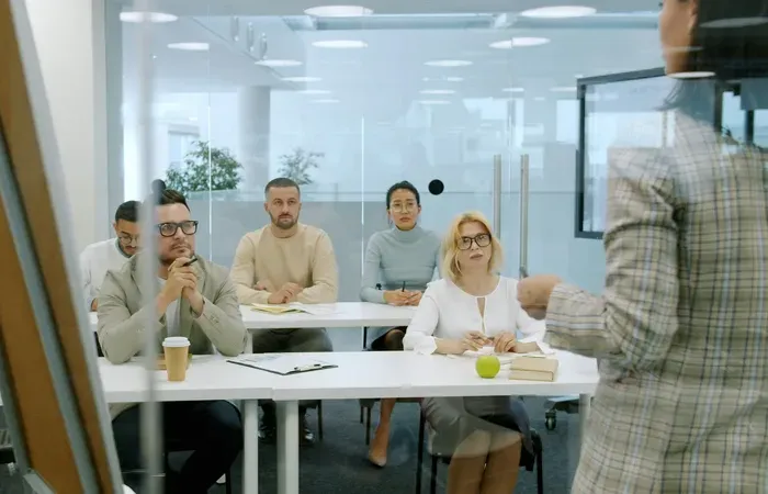 Group of professionals seated in a glass-walled meeting room listening to a presenter during training for Town Service Map
